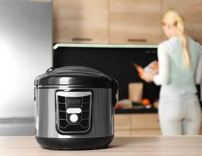 Modern multi cooker and blurred woman on background, space for text