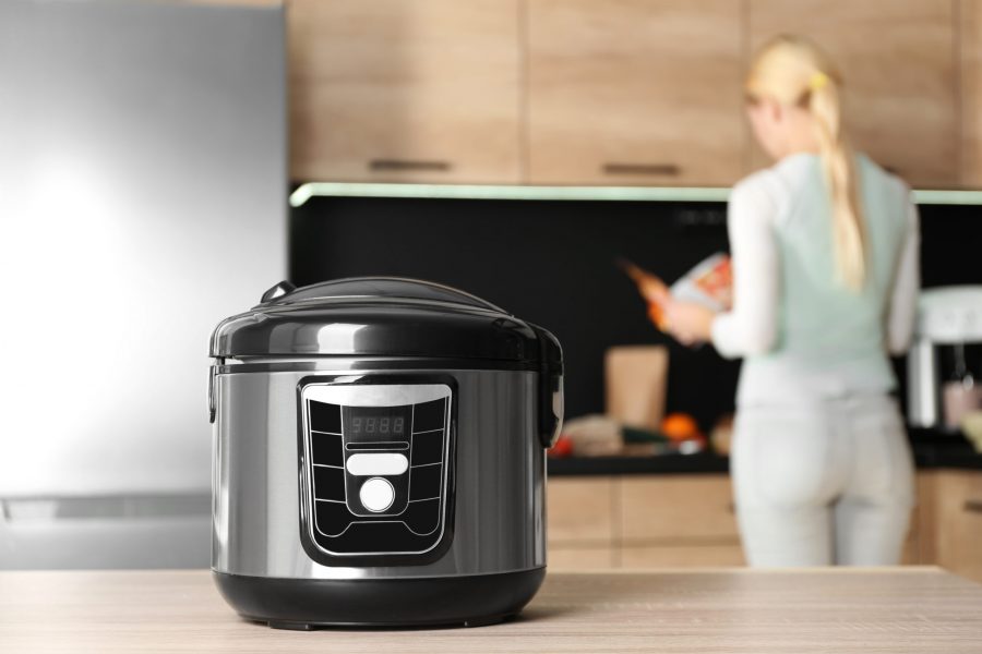 Modern multi cooker and blurred woman on background, space for text