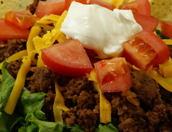 Homemade Mexican Meal: Taco Salad on blue fiesta style plate. Ground beef on bed of lettuce with corn chips, tomatoes, shredded cheddar cheese and sour cream.