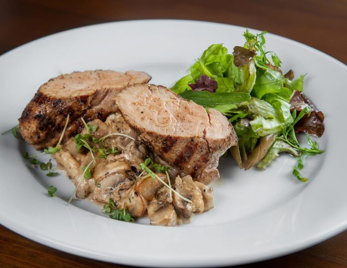 Fillet of pork grilled with mushrooms and cream soum. Dish lies on a plate dyeing lettuce